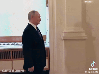 A Man In A Suit And Tie Is Standing In Front Of A White Wall . GIF
