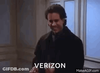 A Man In A Suit And Tie Is Standing In Front Of A Window And Holding A Verizon Phone . GIF