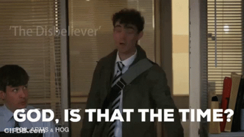 A Man In A Suit And Tie Is Standing In Front Of A Window And Says God Is That The Time GIF