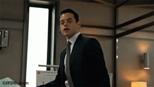 A Man In A Suit And Tie Is Standing In Front Of A Window . GIF
