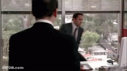 A Man In A Suit And Tie Is Standing In Front Of A Window Looking Out GIF