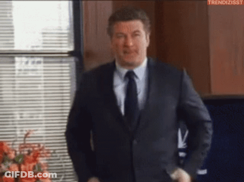 Man In Suit And Tie Standing In Front Of Window With Blinds GIF