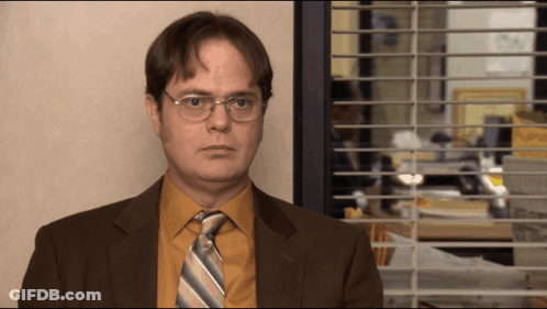 A Man In A Suit And Tie Is Standing In Front Of A Window With Blinds GIF