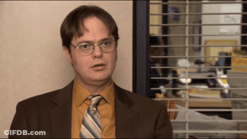 A Man In A Suit And Tie Is Standing In Front Of A Window With Blinds GIF