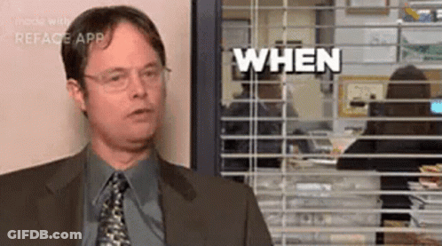A Man In A Suit And Tie Is Standing In Front Of A Window With Blinds And Says `` When '' . GIF