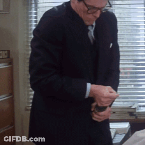 A Man In A Suit And Tie Is Standing In Front Of A Window With Blinds That Says ' A ' On It GIF
