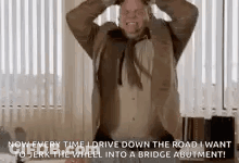 A Man In A Suit And Tie Is Standing In Front Of A Window With His Hands In His Hair . GIF