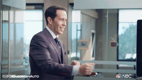 A Man In A Suit And Tie Is Standing In Front Of A Window With The Nbc Logo On The Bottom GIF