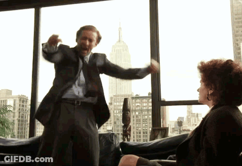 A Man In A Suit And Tie Is Standing In Front Of A Woman In A Chair GIF
