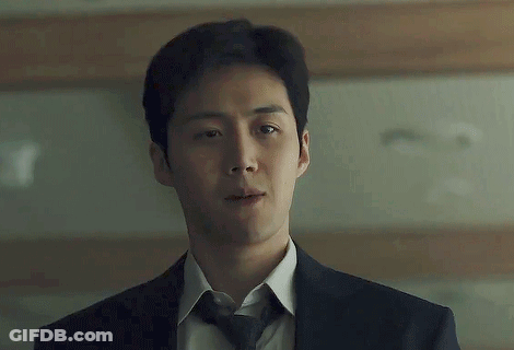 A Man In A Suit And Tie Is Standing In Front Of A Wooden Wall . GIF