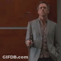 A Man In A Suit And Tie Is Standing In Front Of A Wooden Wall Holding A Cell Phone . GIF