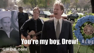 A Man In A Suit And Tie Is Standing In Front Of A Wreath That Says ' You 'Re My Boy Drew ' GIF