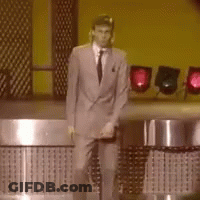 A Man In A Suit And Tie Is Standing In Front Of A Yellow Wall GIF