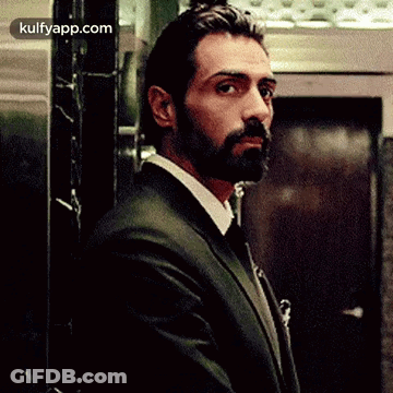 A Man In A Suit And Tie Is Standing In Front Of An Elevator Looking At The Camera . GIF
