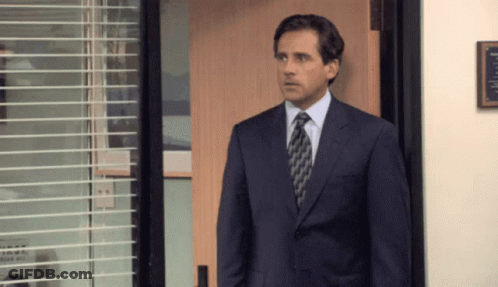 A Man In A Suit And Tie Is Standing In Front Of An Open Door GIF