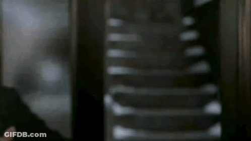 A Man In A Suit And Tie Is Standing In Front Of Stairs . GIF