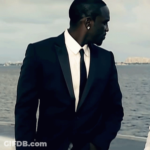 A Man In A Suit And Tie Is Standing In Front Of The Water GIF