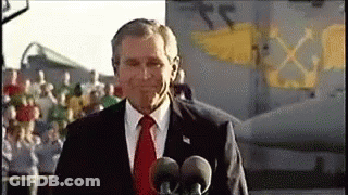 A Man In A Suit And Tie Is Standing In Front Of Two Microphones In Front Of A Plane . GIF