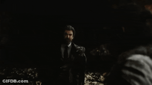 A Man In A Suit And Tie Is Standing In The Dark And Looking At Another Man . GIF