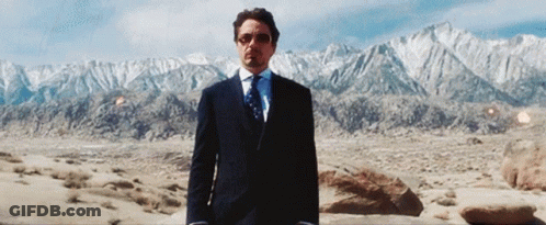 A Man In A Suit And Tie Is Standing In The Desert With Mountains In The Background GIF