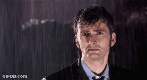 A Man In A Suit And Tie Is Standing In The Rain Looking Sad GIF