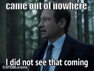 A Man In A Suit And Tie Is Standing In The Woods Looking At Something . GIF