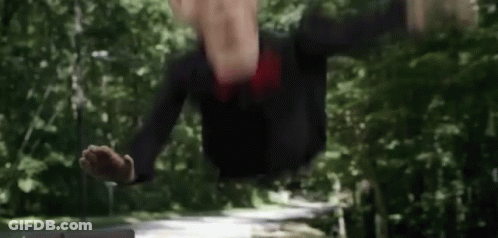 A Man In A Suit And Tie Is Standing In The Woods With His Hands Outstretched . GIF