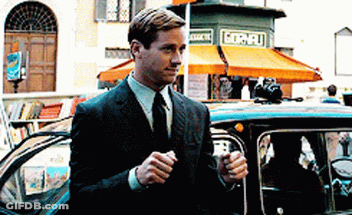 A Man In A Suit And Tie Is Standing Next To A Car In Front Of A Store That Says Gornelli GIF