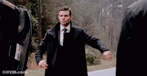 A Man In A Suit And Tie Is Standing Next To A Man In A Black Coat . GIF