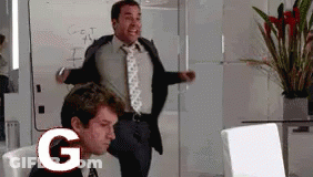 A Man In A Suit And Tie Is Standing Next To A Man In A Chair With The Letter G In Front Of Him GIF