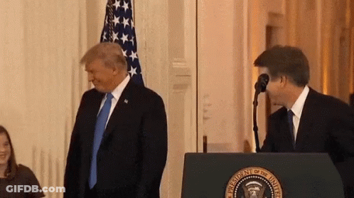 A Man In A Suit And Tie Is Standing Next To A Man In A Suit Behind A Podium . GIF