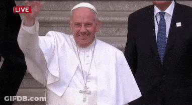 A Man In A Suit And Tie Is Standing Next To A Man In A White Robe Waving . GIF