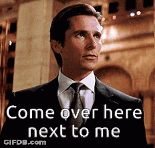 A Man In A Suit And Tie Is Standing Next To A Sign That Says Come Over Here Next To Me GIF