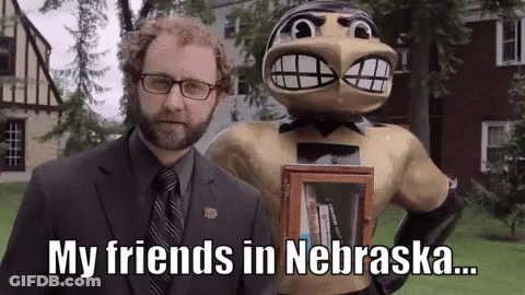 A Man In A Suit And Tie Is Standing Next To A Statue Of A Man With A Beard Holding A Book . GIF