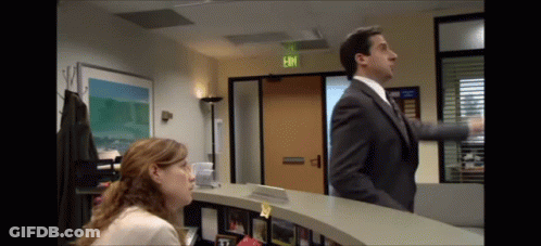 A Man In A Suit And Tie Is Standing Next To A Woman At A Reception Desk In Front Of An Exit Sign GIF
