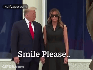 A Man In A Suit And Tie Is Standing Next To A Woman In A Black Dress Holding Hands . GIF