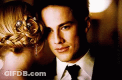 A Man In A Suit And Tie Is Standing Next To A Woman In A Braided Bun GIF