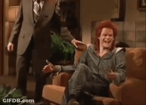 A Man In A Suit And Tie Is Standing Next To A Woman In A Chair . GIF