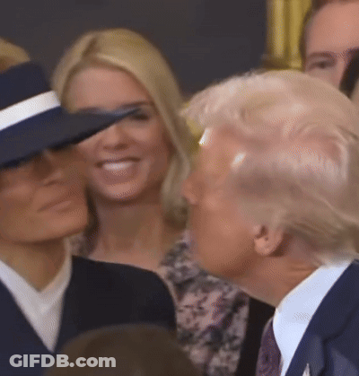 A Man In A Suit And Tie Is Standing Next To A Woman In A Hat GIF