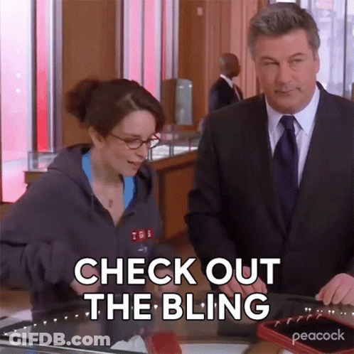 Man In Suit And Tie Next To Woman In Hoodie Saying Check Out The Bling GIF