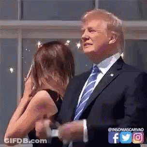 A Man In A Suit And Tie Is Standing Next To A Woman Who Is Covering Her Face . GIF