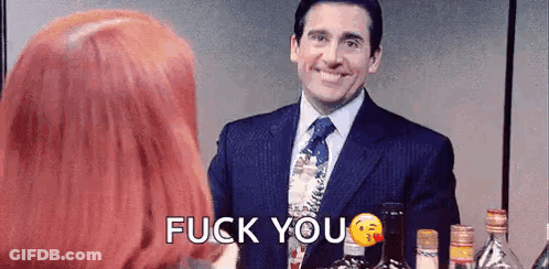 A Man In A Suit And Tie Is Standing Next To A Woman With Red Hair And Says `` Fuck You '' . GIF