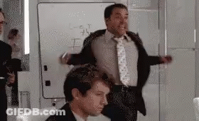A Man In A Suit And Tie Is Standing Next To Another Man In A Chair In Front Of A Whiteboard . GIF