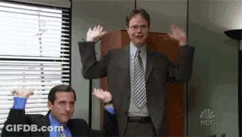A Man In A Suit And Tie Is Standing Next To Another Man In A Chair . GIF
