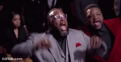 A Man In A Suit And Tie Is Standing Next To Another Man In A Red Suit . GIF