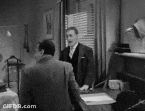 A Man In A Suit And Tie Is Standing Next To Another Man In A Room . GIF