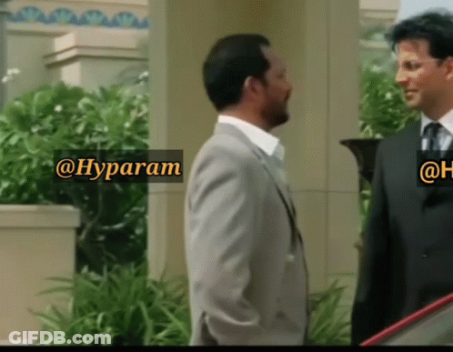 A Man In A Suit And Tie Is Standing Next To Another Man In A Suit And Tie With A Sign That Says @Hyparam GIF