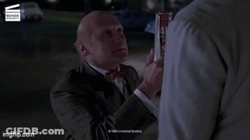 A Man In A Suit And Tie Is Standing Next To Another Man With The Words Slacker On The Screen GIF