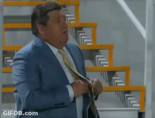A Man In A Suit And Tie Is Standing Next To Stairs GIF