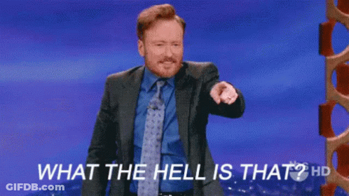 A Man In A Suit And Tie Is Standing On A Stage And Pointing At The Camera . GIF